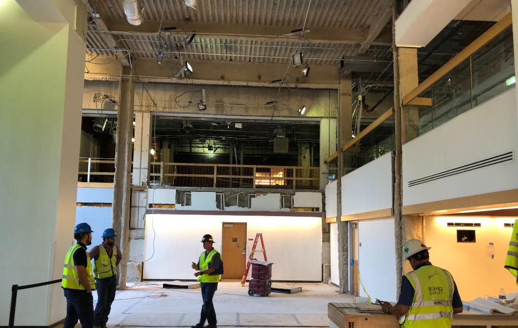 Exposed structural steel framing supporting a large horizontal atrium opening in a commercial building under construction.